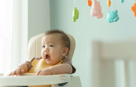 Portrait of Asian little cute baby boy sitting in high chair while waiting for his Mother feeding food at home.の写真素材
