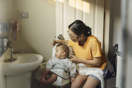 Asian Mother cutting hair her little son by herself with hair clipper in the bathroom at home.の写真素材