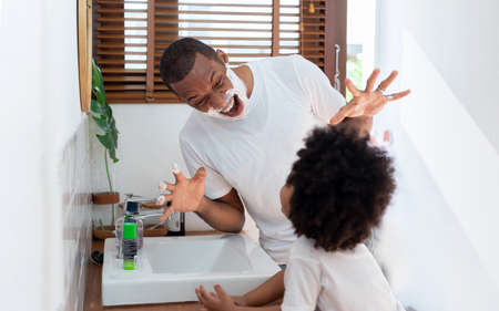 African American Father and little boy playing shaving foam together in bathroom at home together, Black Family having fun.の写真素材