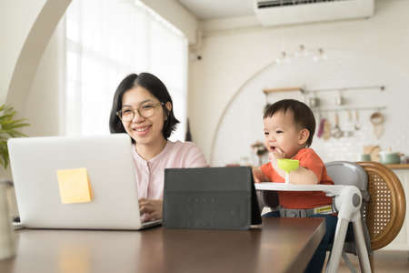 Happy smiling Asian Young mother and little son using laptop together. Mom works from home office.の写真素材
