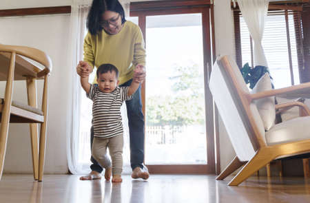 Asian Little toddler boy learning to walk, Mother support and care, Young Mom assisting her son make...