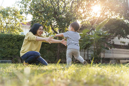 Happy Asian Young mother playing with son outdoor, First steps of the baby, Learning to walk, Little boy running into mom embrace.の写真素材