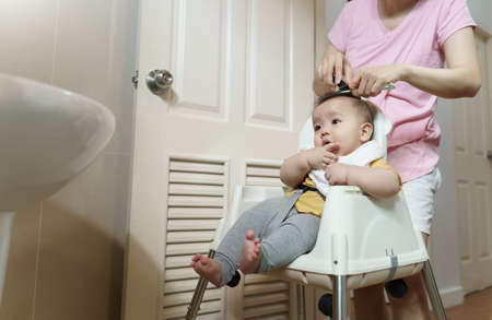 Asian Little baby having haircut with his mother in bathroom at home.の写真素材