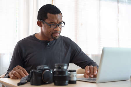 Serious African American photographer man using laptop computer, Black Freelancer working at home studio.の写真素材