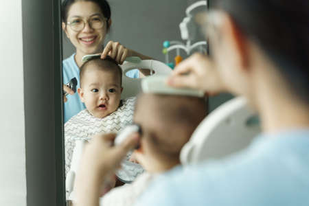 Smiling Asian Mother cutting and trimming her little baby boy hair at home.の写真素材