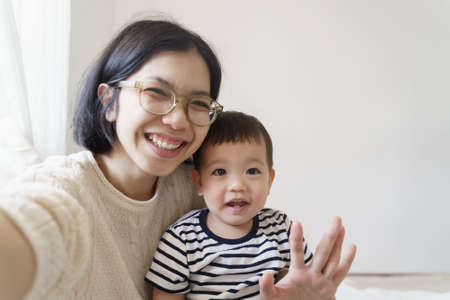 Smiling Chinese Young mother and her little cute boy making video call on using smartphone at home, Asian family taking selfie on mobile phone.の写真素材