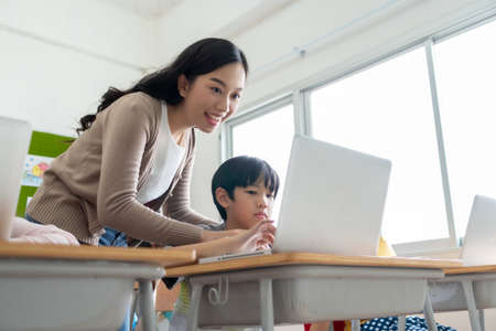 Asian woman teacher is teaching and advice little boy learning on laptop computer at school.の写真素材