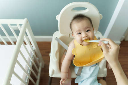 Mother feeding food Cute Asian little baby boy on high chair at home.の写真素材