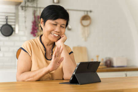 Portrait of Happy smiling Asian senior woman using digital tablet computer waving hand, Online Video call with family.の写真素材