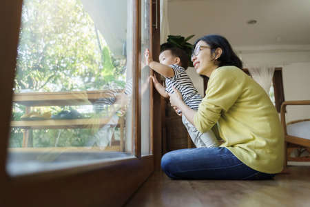Beautiful Young Asian mother and Little son looking out the window at home.の写真素材