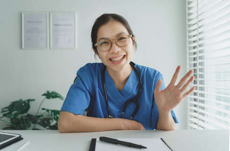 Smiling Asian Female Doctor looking at webcam making conference video call at the hospital.の写真素材