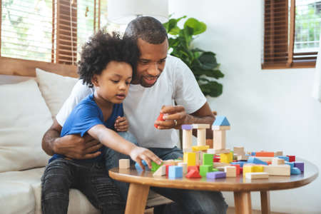 African American Father and his Little son playing building tower with wooden block toy in Living...