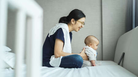 Happy Smiling Asian Young mother and adorable newborn baby sitting on bed doing online video chat with family on smartphone at home.の写真素材