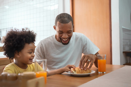 Happy African American Father and little son playing together in breakfast at dining tableの写真素材