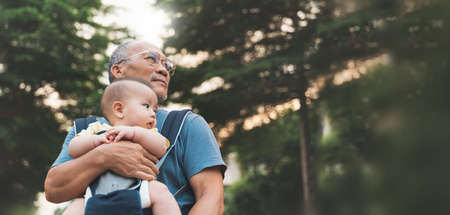 Asian Grandfather carrying his Little Grandson in baby carrier walking at park outdoor, Human relationships.の写真素材