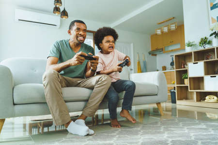 Excited Black Boy sitting on sofa playing video games with his African American Father.の写真素材
