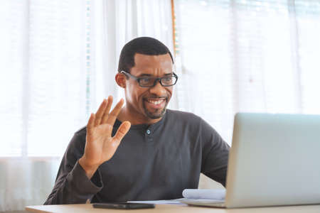 Happy african american man smiling face waving hand talking to webcam, Black male making video call at home.の写真素材