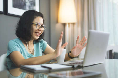 Attractive smiling young Asian woman waving hands on a video call, Young female studying on laptop computer.の写真素材