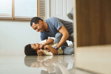 Happy African Father and little Afro boy playing at the floor together, Smiling Dad embracing or cuddling his sonの写真素材
