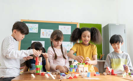 Group Of Multi ethnic Elementary School Pupils playing wooden block toys in Classroom together,...