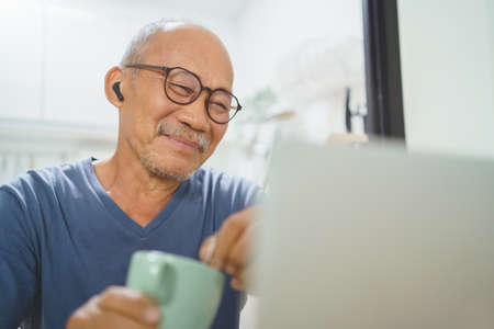 Joyful relaxed Asian Senior Adult man using laptop at home, Smiling face, Chinese male having online Video callの写真素材