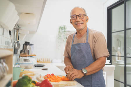 Portrait of Happy retired Asian senior man standing while cooking in kitchenの写真素材