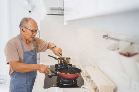Happy Asian Mature adult man wearing eyeglasses cooking in kitchen, Prepare Food.の写真素材
