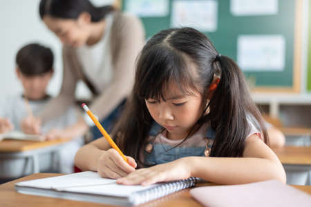 Concentrated Little School Girl studying in classroom at the primary international school.