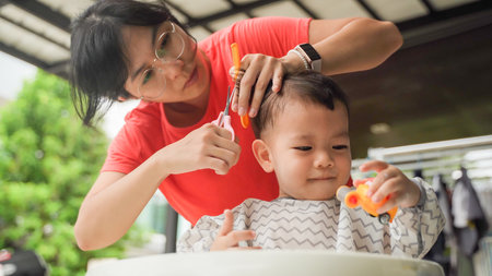 Asian Mother cutting her Little son's hair at home outdoor, Adorable boy having fun.の写真素材
