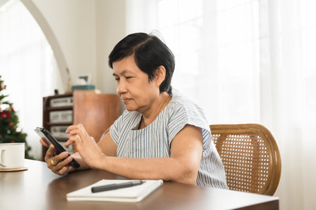 Asian Senior mature female sitting using smartphone at home.の写真素材