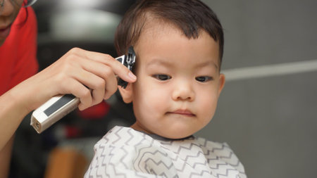 Asian Little toddler boy getting haircut by his parent with hair clipper at outdoorの写真素材