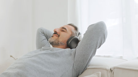 Happy relaxed Mature Adult man in headphones listening to the music and resting sitting on...