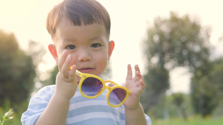 Portrait of Happy Asian little boy in yellow sunglasses looking at camera outdoorの写真素材