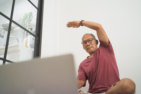 Asian senior Adult man training and stretching arm with Laptop, Home Workout exercises, Healthy lifestyle conceptの写真素材