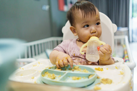 Little Toddler Asian baby boy with messy face sitting in high chair eating and drinking water.の写真素材