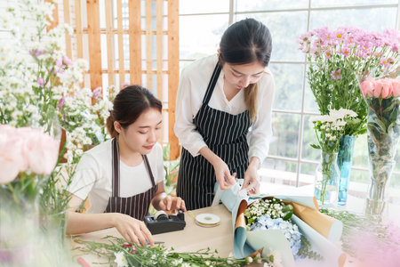 Two Asian female florists preparing and arranging and wrapping bouquet flowers at flower shop. Small business owner, entrepreneurの写真素材
