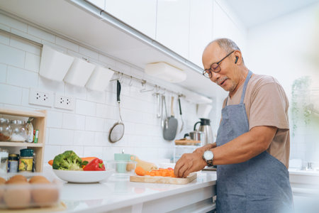 Happy smiling Asian Senior adult man chopping carrots on wooden board, Japanese or Chinese Mature Male cooking in kitchen, Preparing food.の写真素材