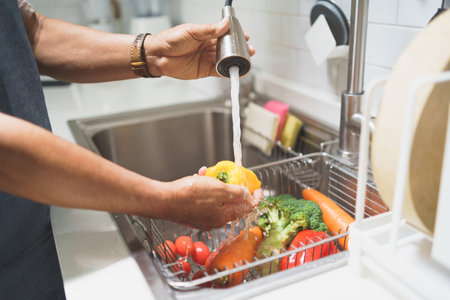 Closeup senior man hands washing and cleaning bell pepper and other vegetable in the kitchen sinkの写真素材