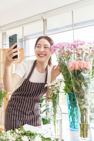 Happy Beautiful Asian Chinese woman florist taking selfie with smartphone in flower shop, Small business owner, entrepreneur, Using mobile phone, Verticalの写真素材