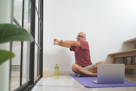 Chinese middle aged man sitting on yoga mat exercising at home, Stretching arms, Workoutの写真素材