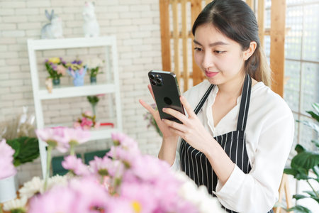 Pretty Asian Chinese woman florist taking photo of bouquet of flowers with smartphone in flower shop, Small business owner, entrepreneur, Using mobile phoneの写真素材