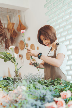 Asian Korean female florist cutting and arranging flowers at home. Trimming tip of stem at Carnation. Small business ownerの写真素材