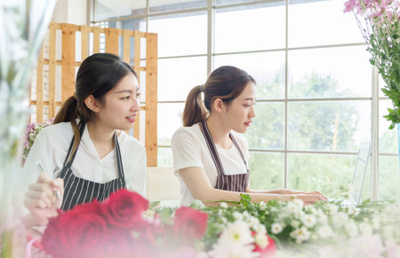 Asian Korean female florists working on laptop in flower store, chatting with clients, Small business, taking customer order, Entrepreneurの写真素材
