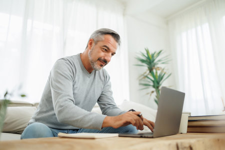 Confident Bearded mature adult man using and typing on laptop, Working at home office, Remote working, freelancerの写真素材