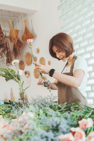 Asian Korean female florist cutting and arranging flowers at home. Trimming tip of stem. Small business ownerの写真素材