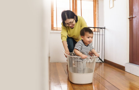 Happy smiling Asian Mother playing with her little adorable son with the basket on the floorの写真素材