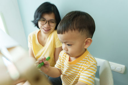 Happy Smiling Asian mother and her little boy coloring with crayon at homeの写真素材