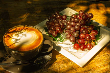 Picture of  cappuccino and red grapes on white plate - text space
