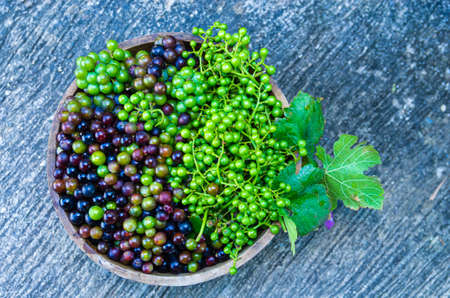 Picture of red and green grapes with unripe grapes in a wooden bowl background cement floor with grooves -  Focus on the grapes - background blurの写真素材