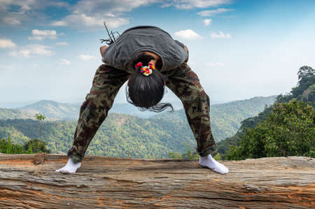 Picture of a woman does exercises on a trunk in the background mountain landscape.